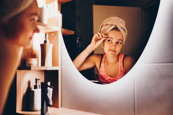 Young white woman plucking her eyebrows