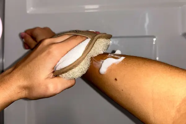 A person uses the Almooni Natural Loofah Exfoliating Body Scrubber on their arm
