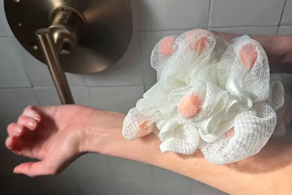 A person scrubs their arm with the ecoTools Lathering EcoPouf Bath Sponge