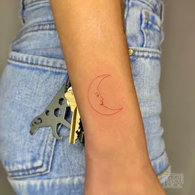 Red crescent moon tattoo with face near wrist