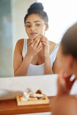 woman picking at face in the mirror