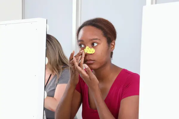 Person looking in mirror while applying Starface Lift Off Pore Strip to their nose