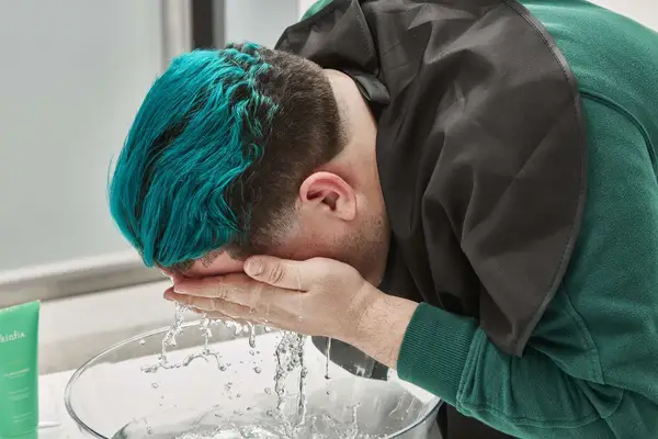 Person rinsing face with water over bowl