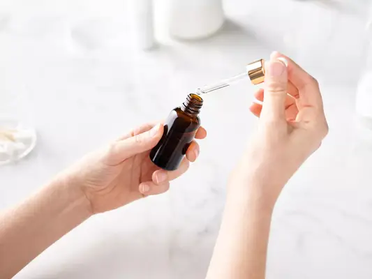 Two hands holding a glass dropper bottle in one hand and the dropper in the other
