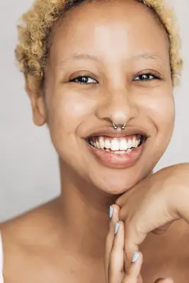 Smiling person with short, blonde curls and septum piercing