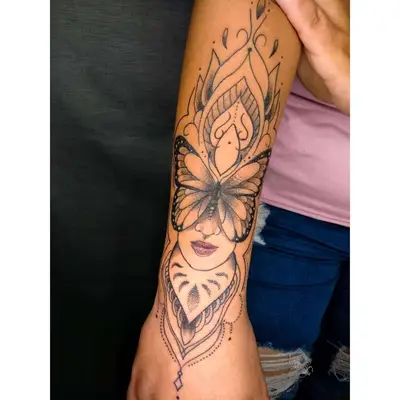 Person with an intricate butterfly and face mandala tattoo on the arm