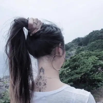 Person lifts hair to reveal intricate mandala tattoo on the back of the neck