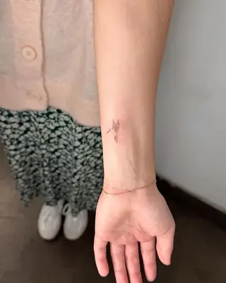 Person with a dainty bird wrist tattoo