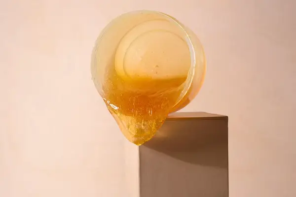 Hard wax dripping out of a tub, on a pale pink background.