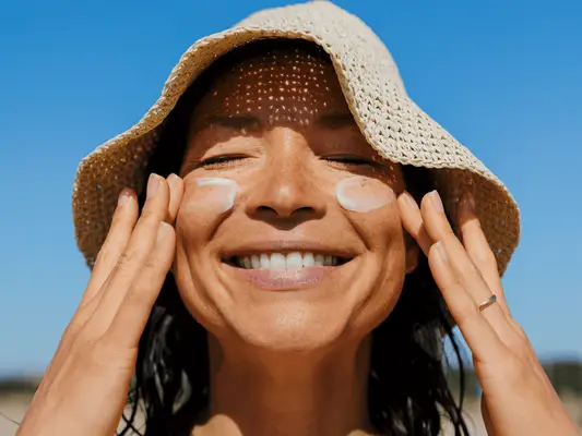 Person applying sunscreen to their face, wearing a straw hat