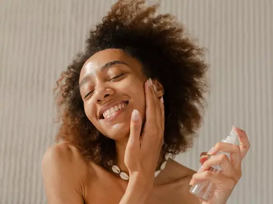 A woman smiling as she sprays her face with a facial mist