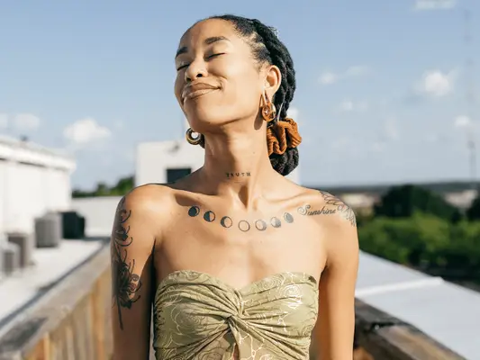 Woman with locs with her eyes closed while taking in the sunshine at a rooftop party.