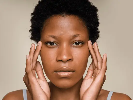 A woman looking straight at the camera with her hands framing both sides of her face