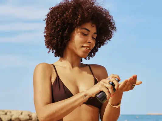 Close up of a model applying product into her hands on the beach.