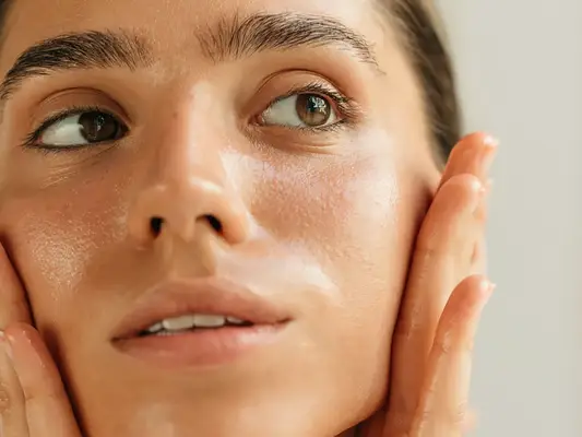 close up of a woman with clear, glowy skin, holding her face