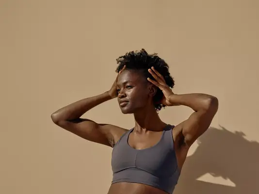 Woman with acne scars holding hair and standing in sports bra