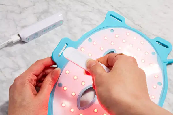 Hands attaching strap to HigherDose Red Light Face Mask