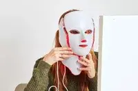 A person wears the CurrentBody Skin LED Light Therapy Mask and neck attachment