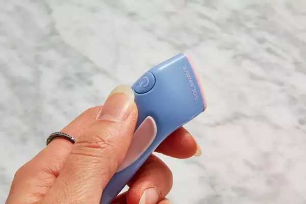 Closeup of hand holding Solawave Bye Acne 3-Minute Pimple Spot Treatment with marble countertop in background