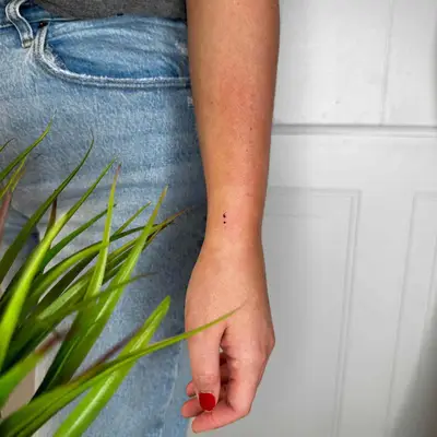 Micro semicolon tattoo on wrist next to jeans and plant