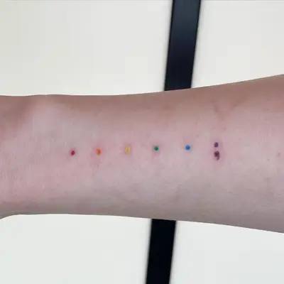 Arm with rainbow dot designs featuring purple semicolon tattoo