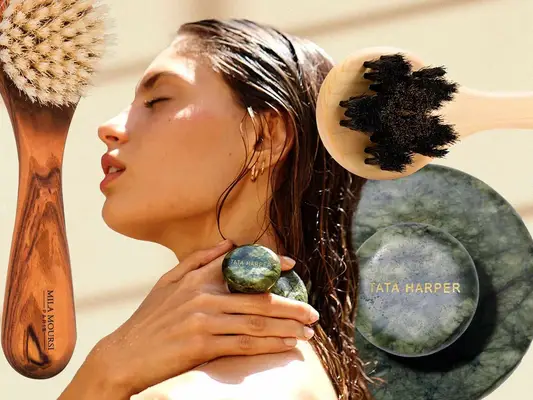 A person using a Tata Harper exfoliating tool with the same item and two exfoliating brushes in the background