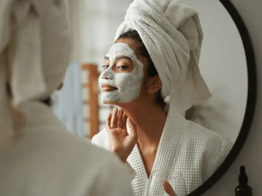 Close up of woman looking in the mirror with face mask having a spa day