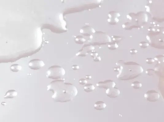 Close up of drops of skincare water on a baby pink background