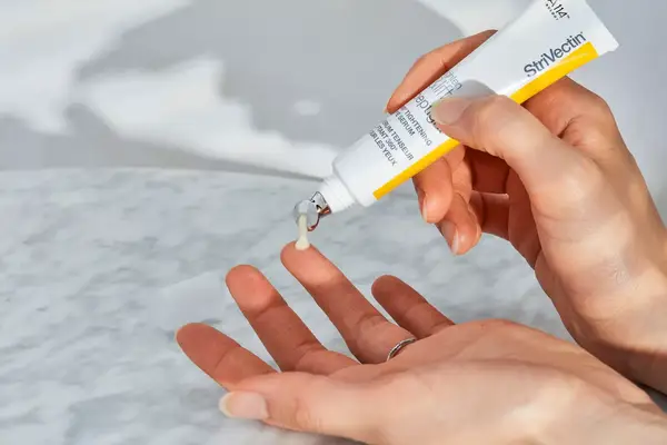 A person applies StriVectin Peptight 360 Tightening Eye Serum to their finger. 