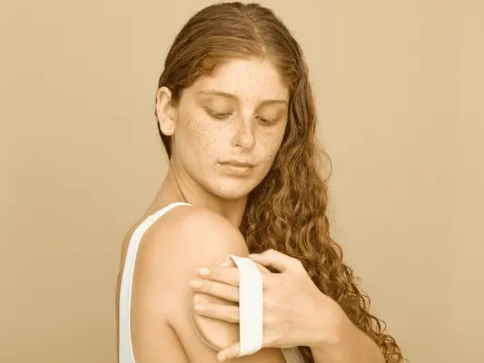 woman using dry brush on arm against tan background