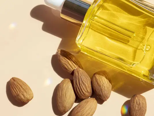 Bottle of skincare oil with pile of whole almonds