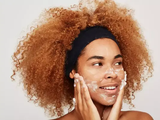 Close up of a black woman with curly red hair washing face.