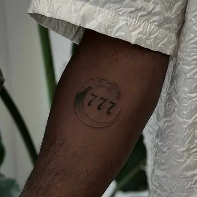 Close-up of fine line wave tattoo with 777 on arm