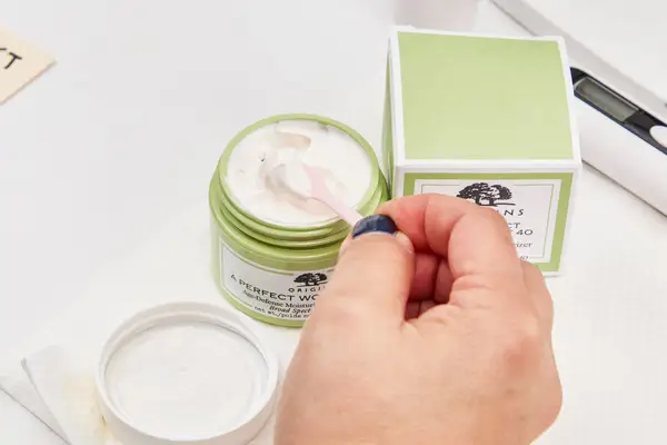 Hand scooping up cream from the Origins A Perfect World SPF 40 Age-Defense Moisturizer With White Tea container