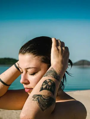 girl with wet hair near a body of water, with tattoos on both arms
