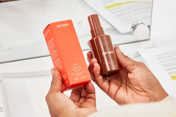 Hands holding the Cay Skin Isle Glow Face Moisturizer SPF 45 bottle and box