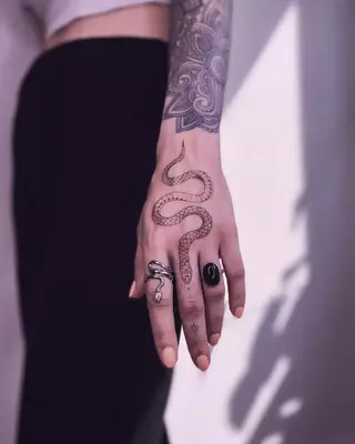 Snake tattoo on hand down the middle finger surrounded by a snake ring and a black ring