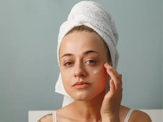Close up of a woman with her hair in a towel applying cream to her face