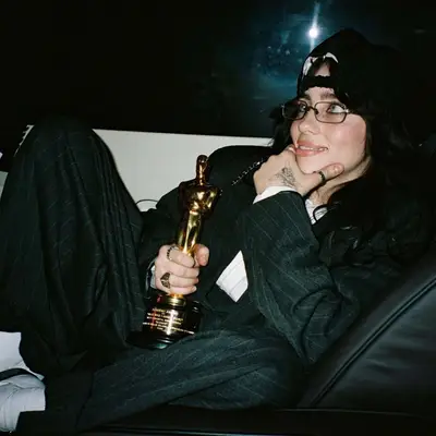 Billie Eilish poses in pinstriped suit while holding her Oscar trophy and showing off her fairy hand tattoo