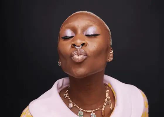 Cynthia Erivo doing a kissing face with a silver nose piercing and purple eyeshadow