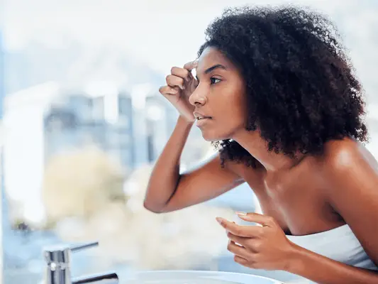 A woman looking in the mirror and touching her forehead
