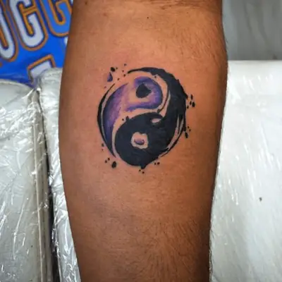 Close up of a purple and black watercolor yin-yang symbol tattoo.