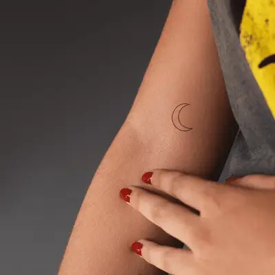 small crescent moon tattoo above crease of arm 
