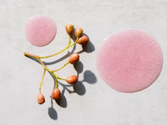 droplet of skincare next to flower on white background