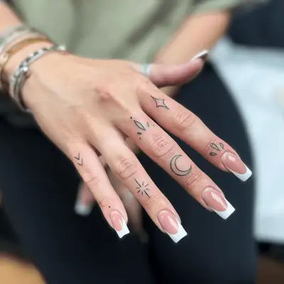 hand with minimalist star and moon tattoos on fingers