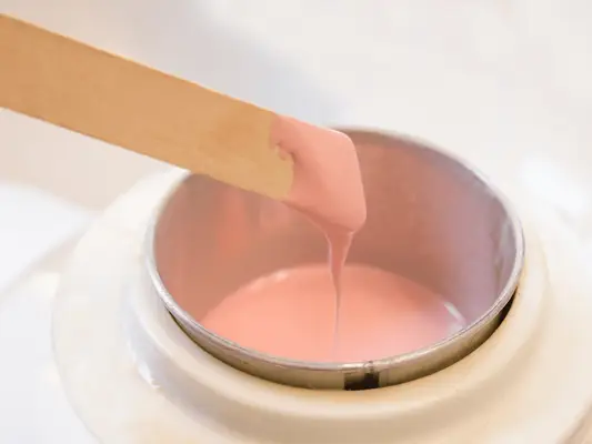Image of a stick with pink wax being warmed in a warmer
