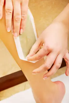 woman peeling waxing strip off leg