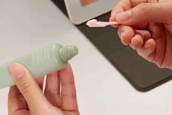 Hands holding a tube of Caudalie Vinopure Moisturizing Mattifying Fluid and a spoon with a dollop of the cream