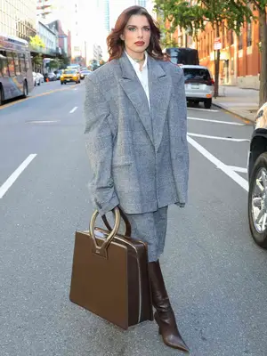 Julia Fox wearing a plaid blazer with a coordinating skirt, brown leather boots, and an oversized brown leather bag