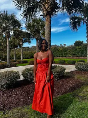 Amber Desiree wears a red drop waist dress outside near palm trees